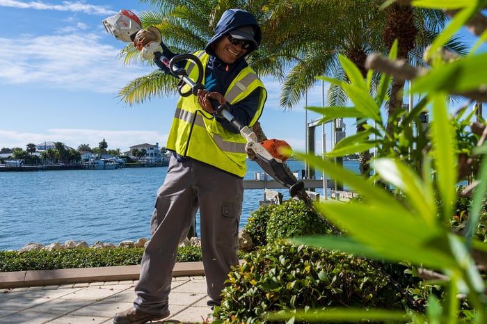 Crew member hedge trimming landscape beds near water 2